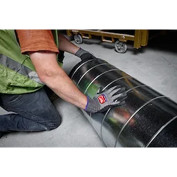 Person wearing Cut Level 7 High-Dexterity Nitrile Dipped Gloves - L, handling a large metallic duct in a construction site.