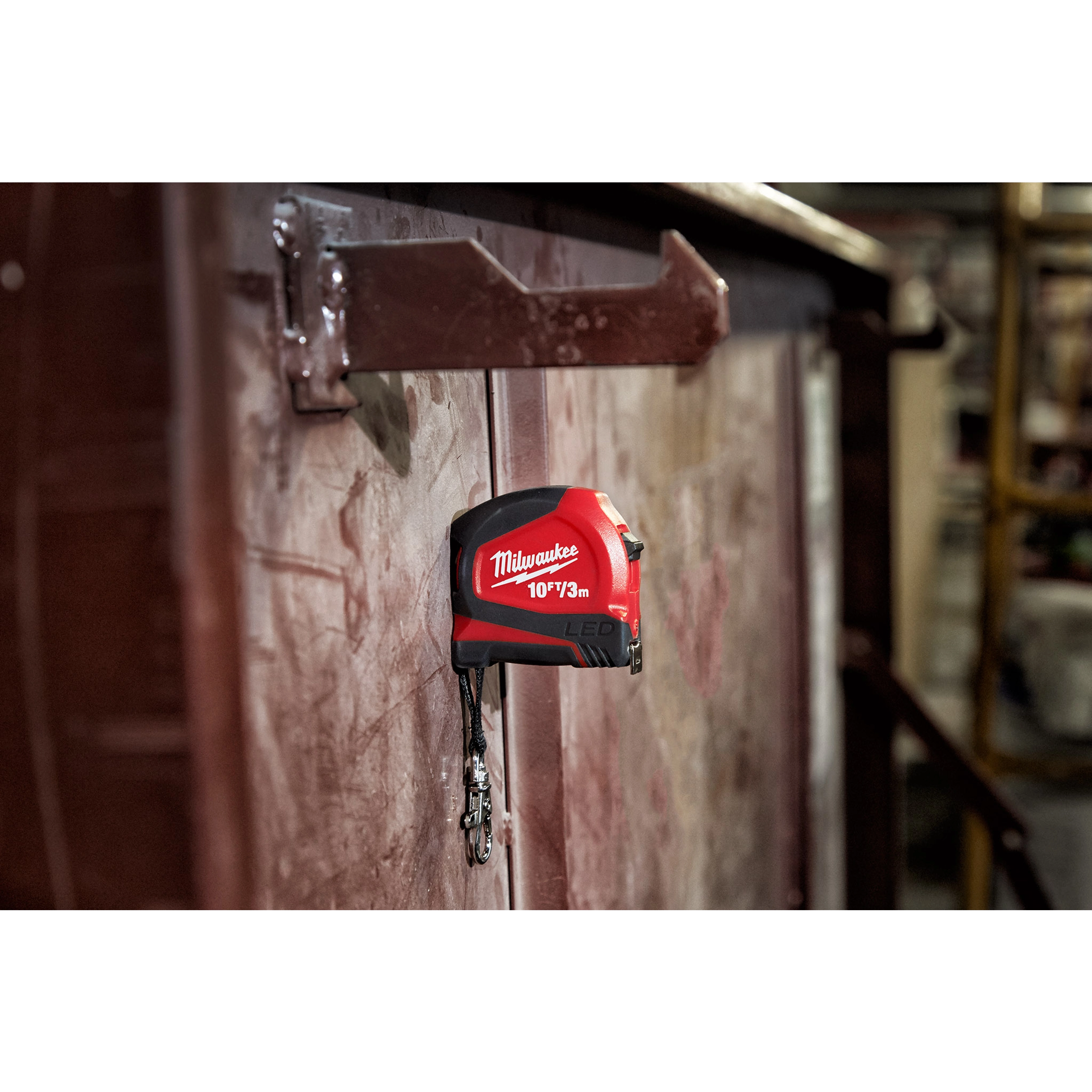 Red and black 10ft/3 Keychain Tape Measure with LED attached to a metallic surface using its magnetic back, keys hanging below.
