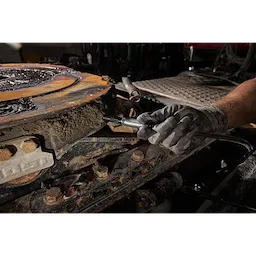 Gloved hand using a Right Angle Grease Coupler on a dirty, rusted metal machinery part.