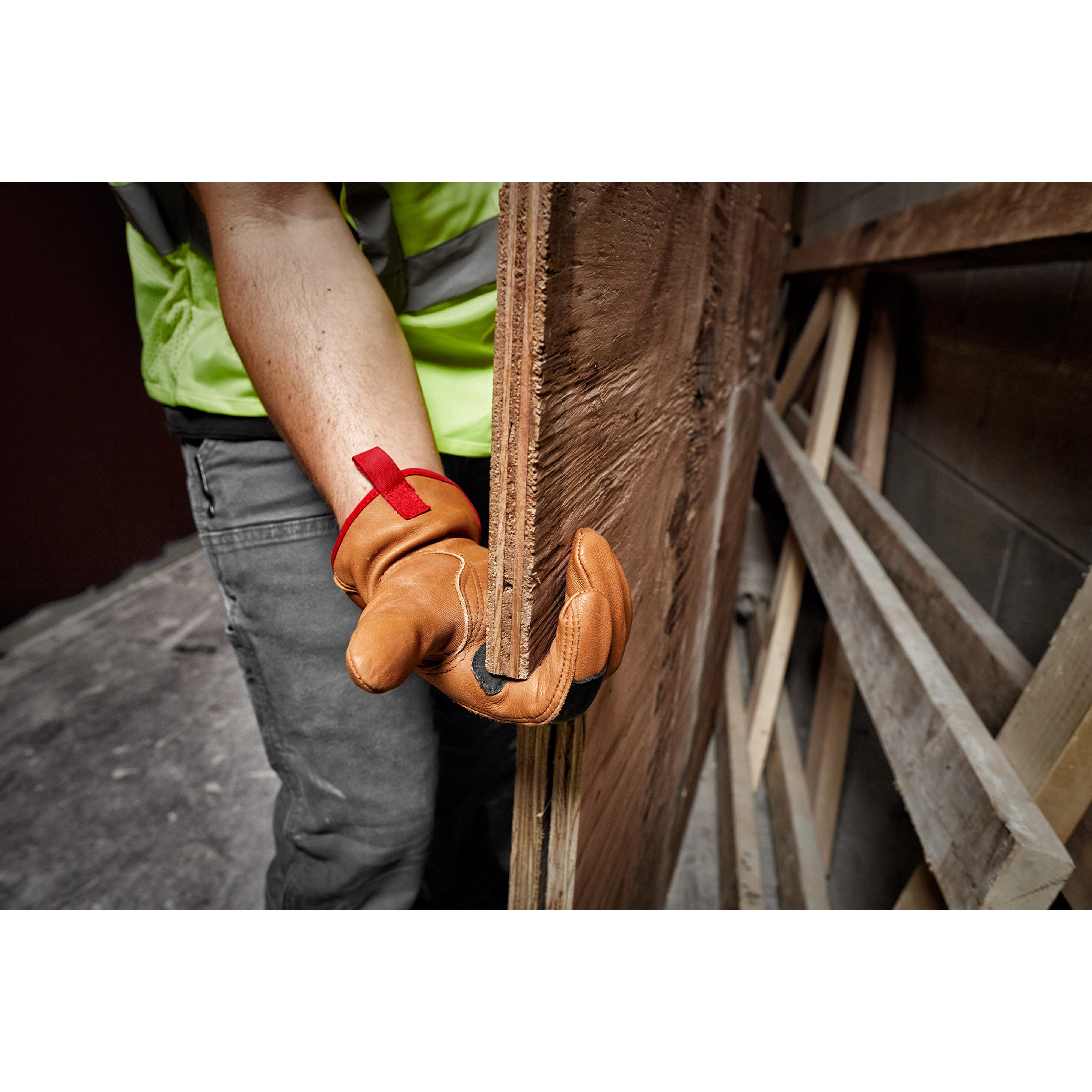 Person wearing Goatskin Leather Gloves, holding a wooden board in a workshop. The gloves are tan with a red pull tab.
