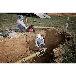 Two workers in safety gear are using the MX FUEL™ Electrofusion Processor on a yellow pipe in a dug-out area. One worker operates the processor while the other monitors on the surface. Equipment and safety cones are visible nearby.