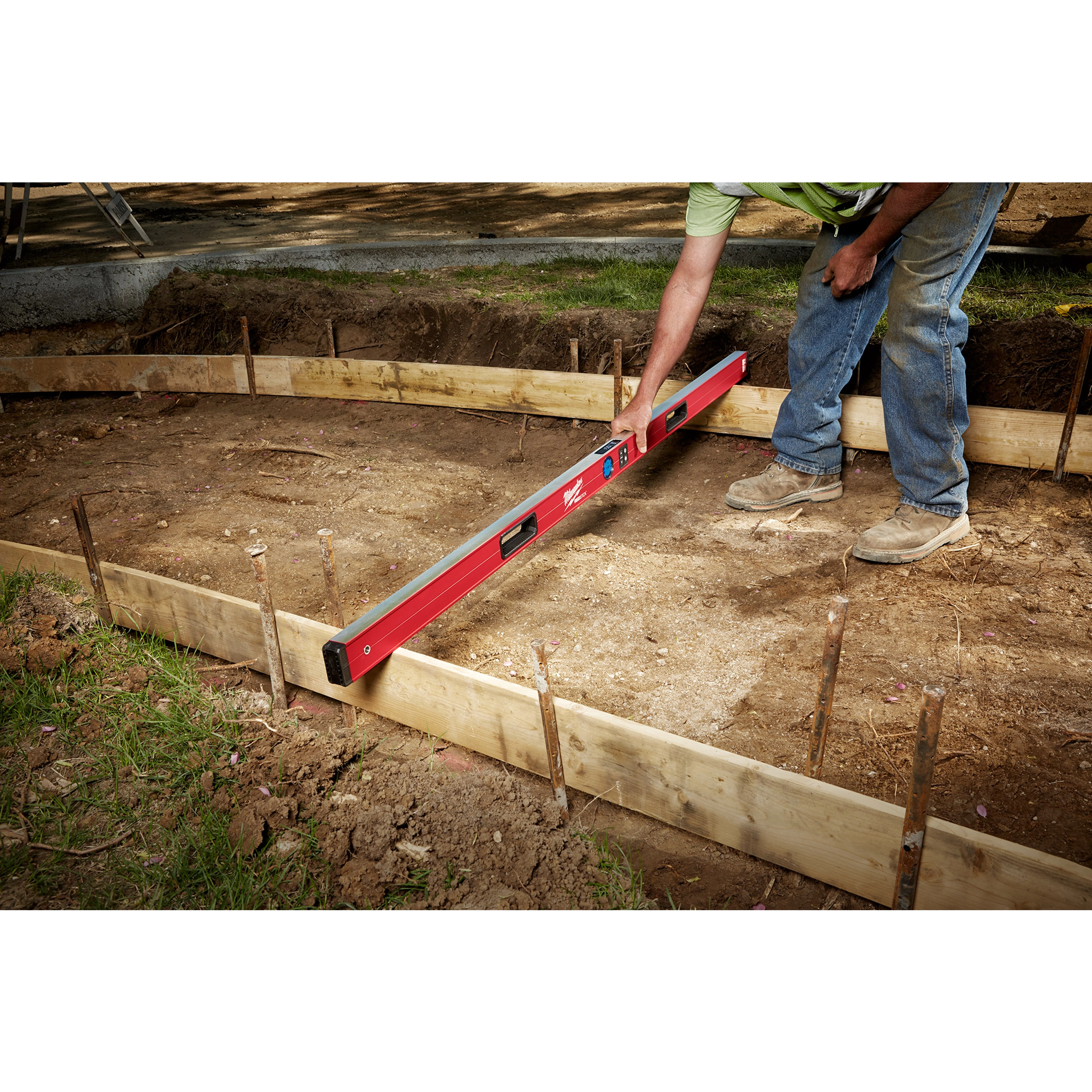 A person uses the Milwaukee REDSTICK Digital Level with PINPOINT Measurement Technology to level the ground at a construction site.