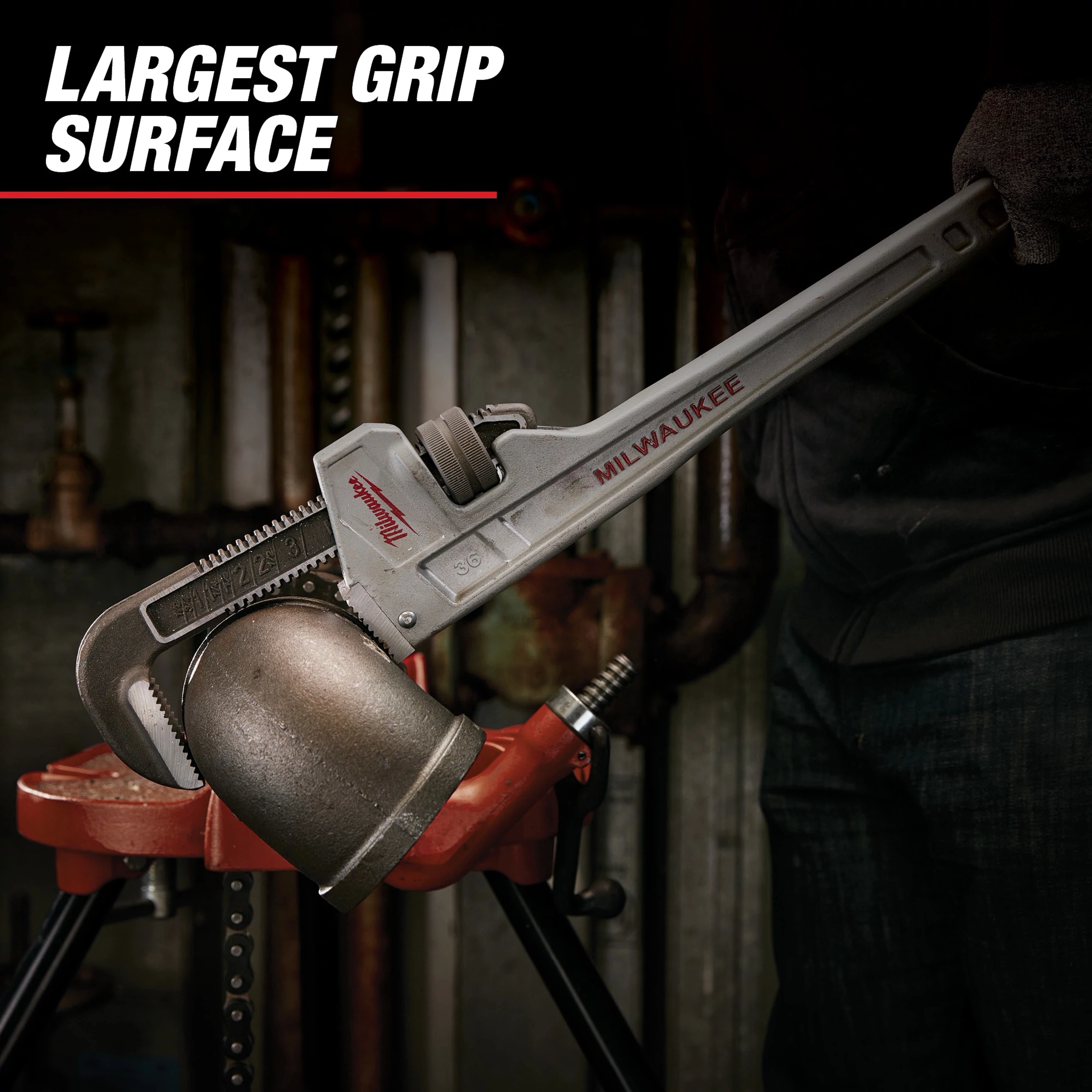 Milwaukee pipe wrench gripping a large metal pipe with the text "Largest Grip Surface" at the top left. The wrench is silver with a red Milwaukee logo and is being used by a person wearing dark clothing.