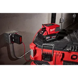 Milwaukee M18 REDLITHIUM XC 5.0 battery is charging on a station. The charger is connected to a power outlet with a red cable and sits on top of a red and black toolbox.