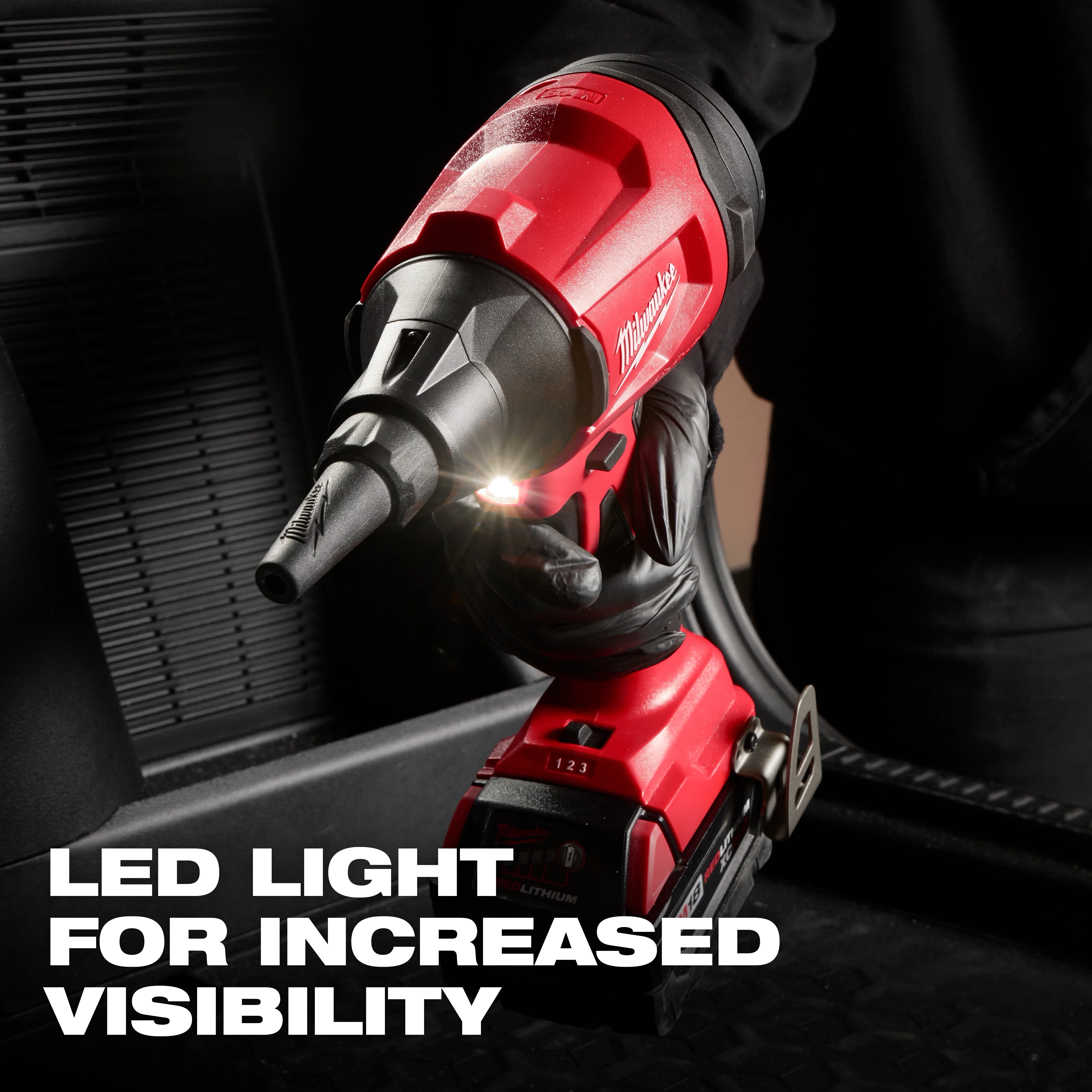 The M18™ Brushless Precision Blower is shown being used, featuring a built-in LED light. The red and black blower has a compact design and is held by a gloved hand. Text overlay states "LED LIGHT FOR INCREASED VISIBILITY."