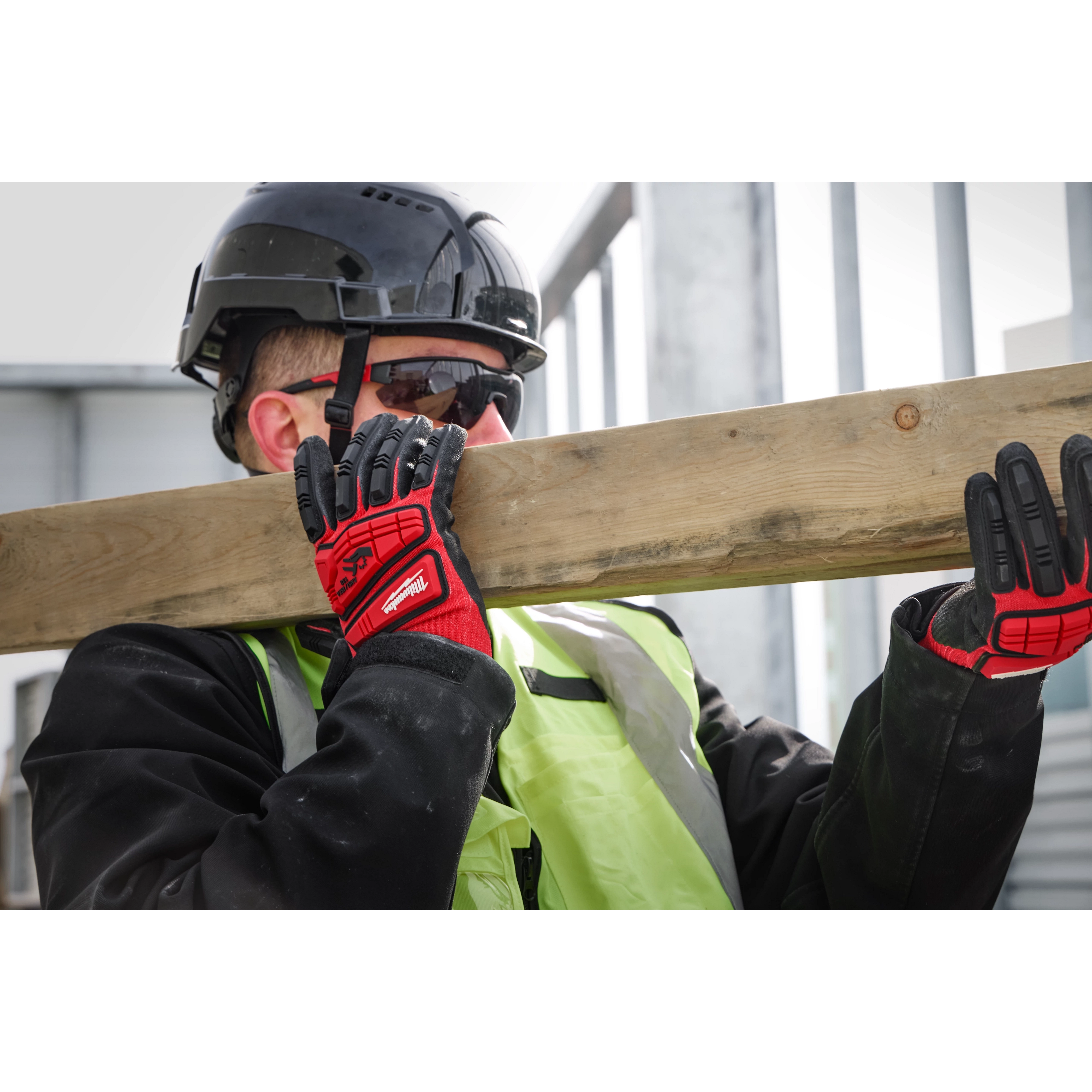 Worker carrying wooden beam, wearing IMPACT CUT 3 NITRILE DIP GLOVE - L, high-visibility vest, and safety helmet at a construction site.