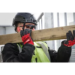 Worker carrying wooden beam, wearing IMPACT CUT 3 NITRILE DIP GLOVE - L, high-visibility vest, and safety helmet at a construction site.