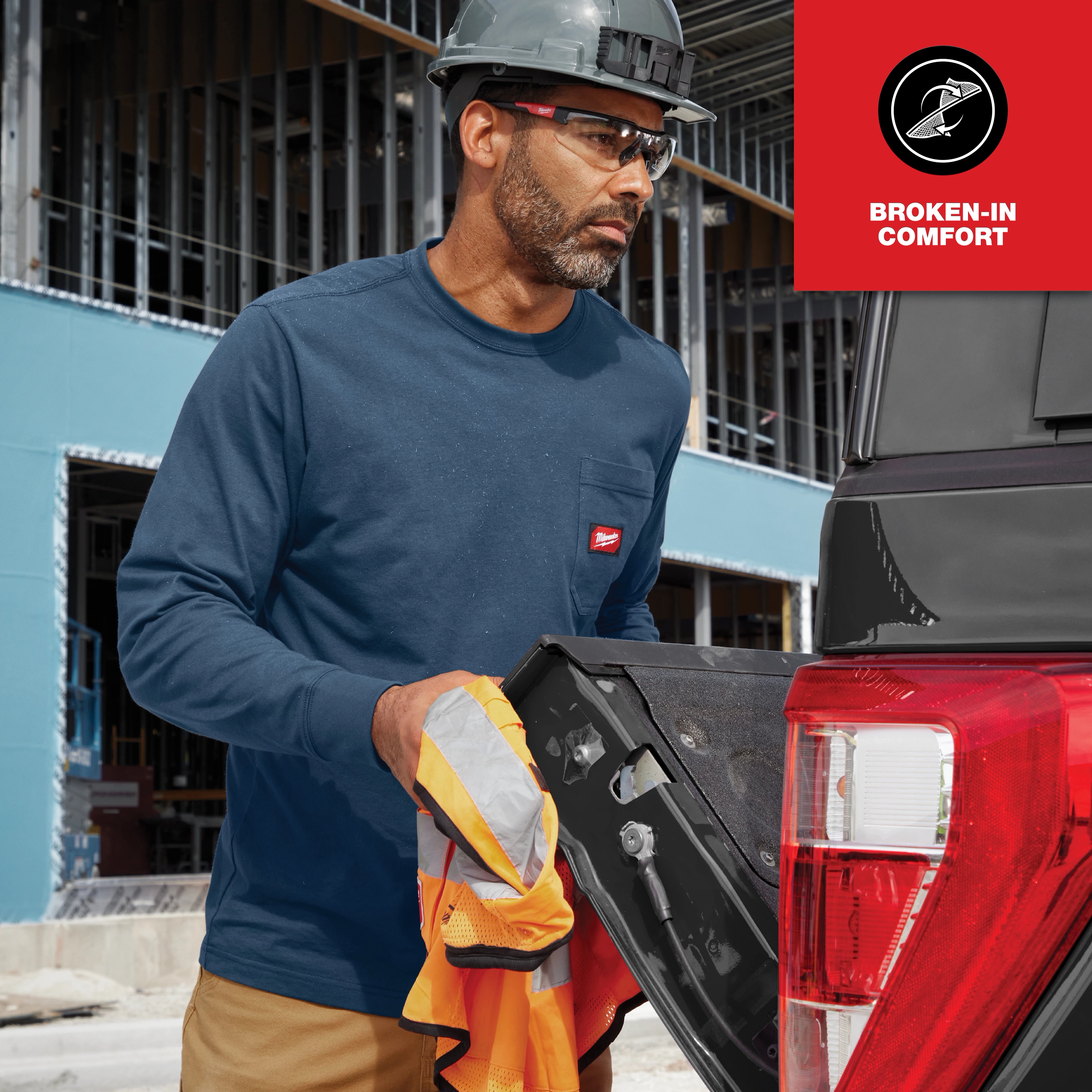 Construction worker wearing a long sleeve, GRIDIRON Pocket T-Shirt with "Broken-in Comfort" label, holding equipment by a truck.