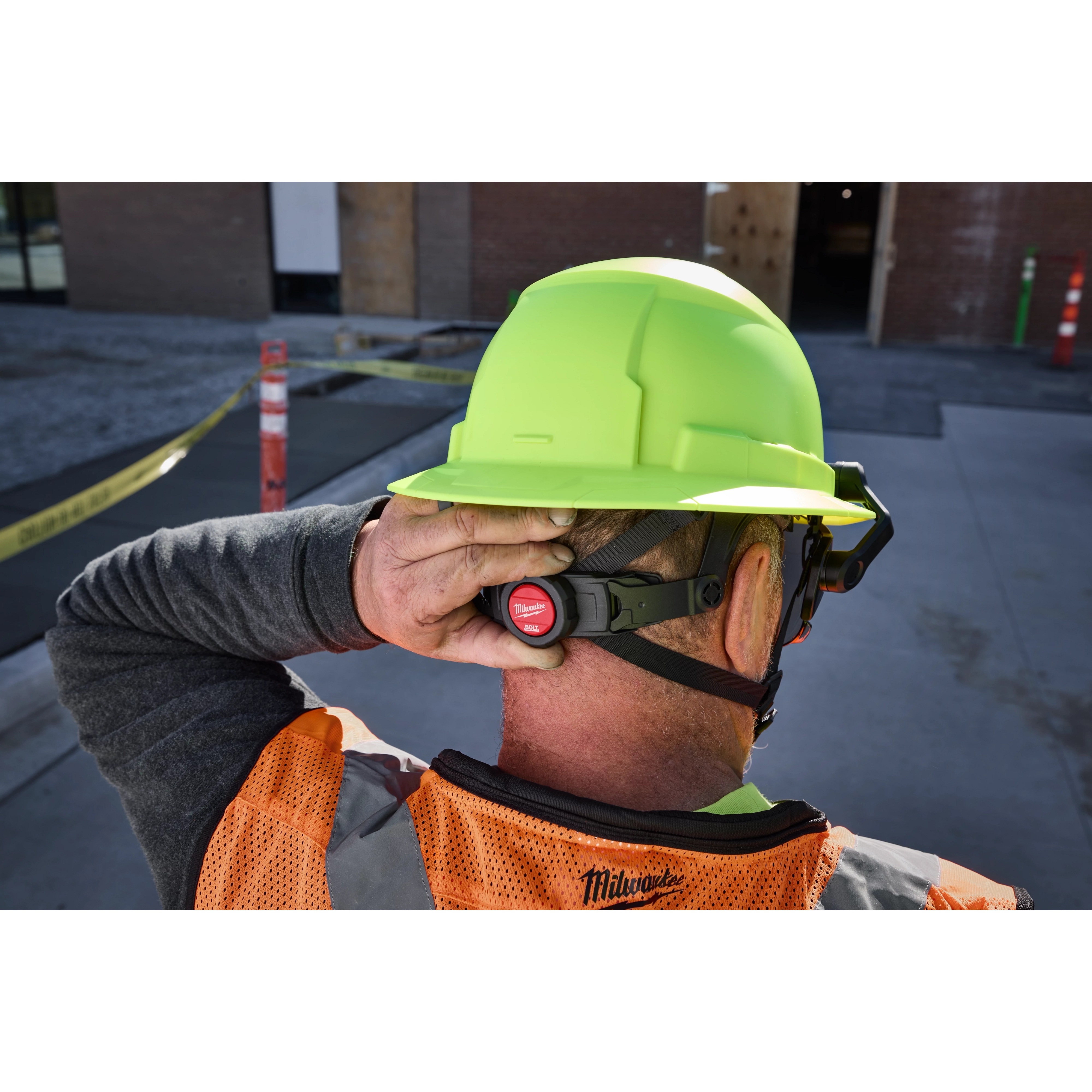 Worker in orange vest adjusts BOLT 4PT High Visibility Green Full Brim Non-Vented Safety Helmet.