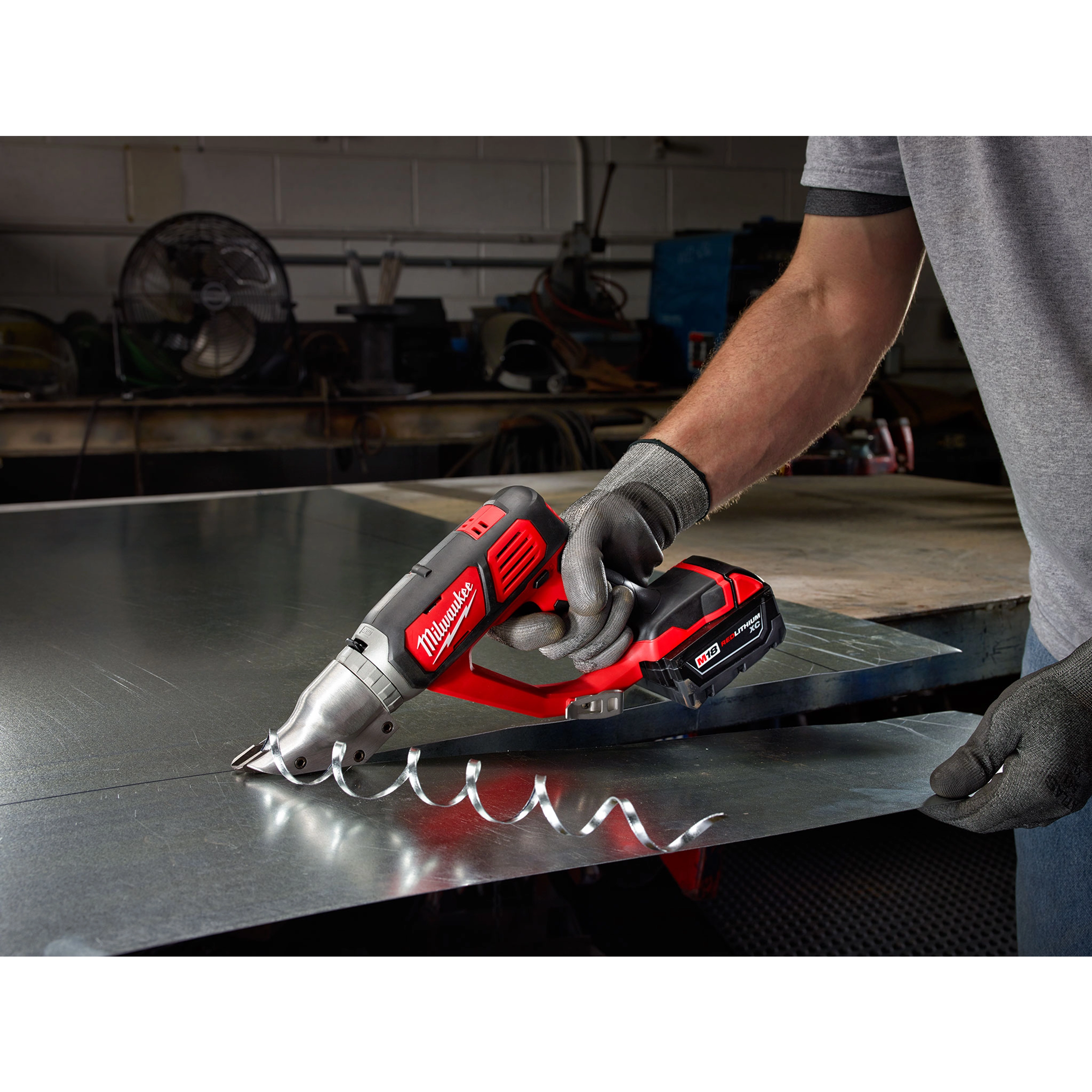 Person using the M18 18 Gauge Double Cut Shear Kit to cut through a sheet of metal, creating a spiral strip of metal waste.