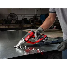 Person using the M18 18 Gauge Double Cut Shear Kit to cut through a sheet of metal, creating a spiral strip of metal waste.