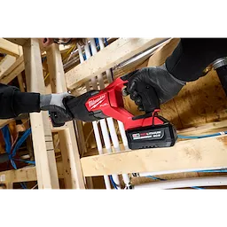 Worker using a red power saw with an M18 REDLITHIUM HIGH OUTPUT XC5 Battery Pack among wooden framing and pipes.