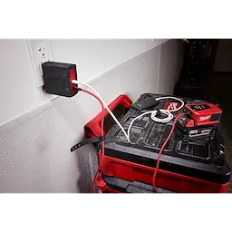 The image displays the Milwaukee 120W USB-C 2-Port Wall Adapter plugged into a wall socket, charging multiple devices.