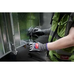A person wearing Cut Level 7 High-Dexterity Nitrile Dipped Gloves - L is manipulating a piece of metal, demonstrating the gloves' protective and flexible nature. The gloves are gray with black palms and display a red and white label on the back of the hand.