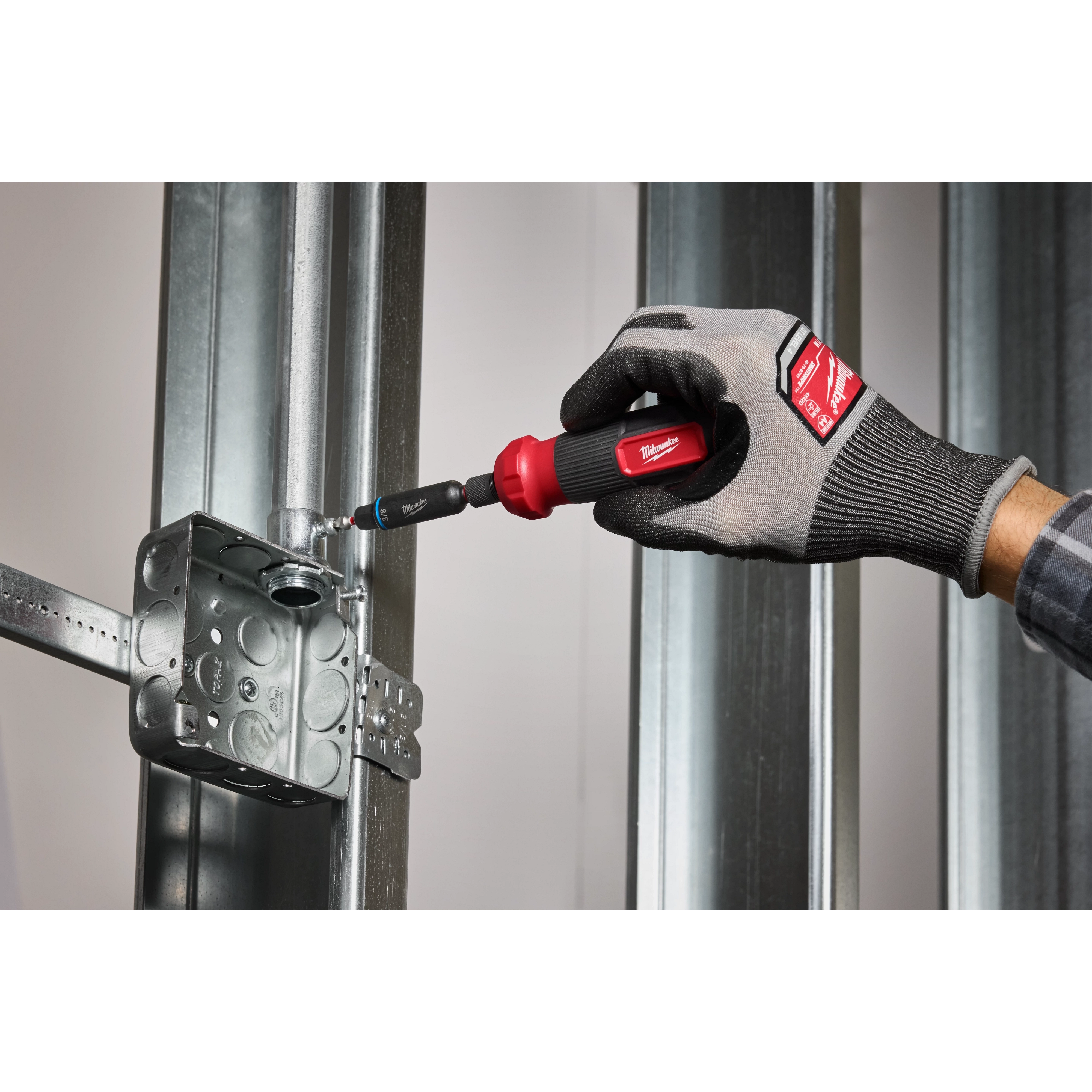 A hand using the Milwaukee 8-IN-1 Multi-Bit & Nut Driver with SHOCKWAVE Impact Duty Bits & Nut Drivers to secure a metal screw into an electrical box mounted on a metal frame.