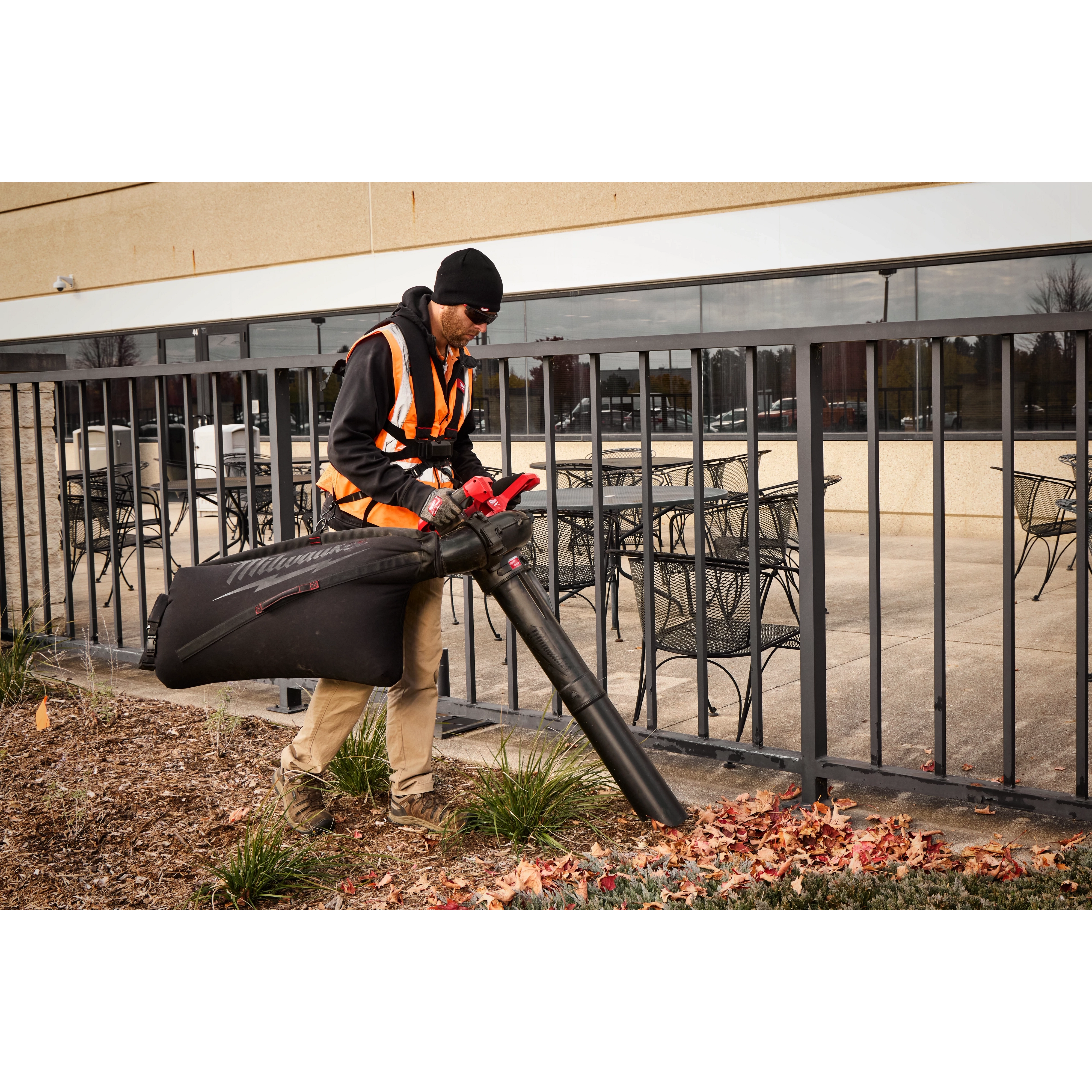 Worker uses an M18 FUEL Dual Battery Mulching Vacuum to collect leaves along a building walkway.