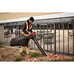 Worker uses an M18 FUEL Dual Battery Mulching Vacuum to collect leaves along a building walkway.