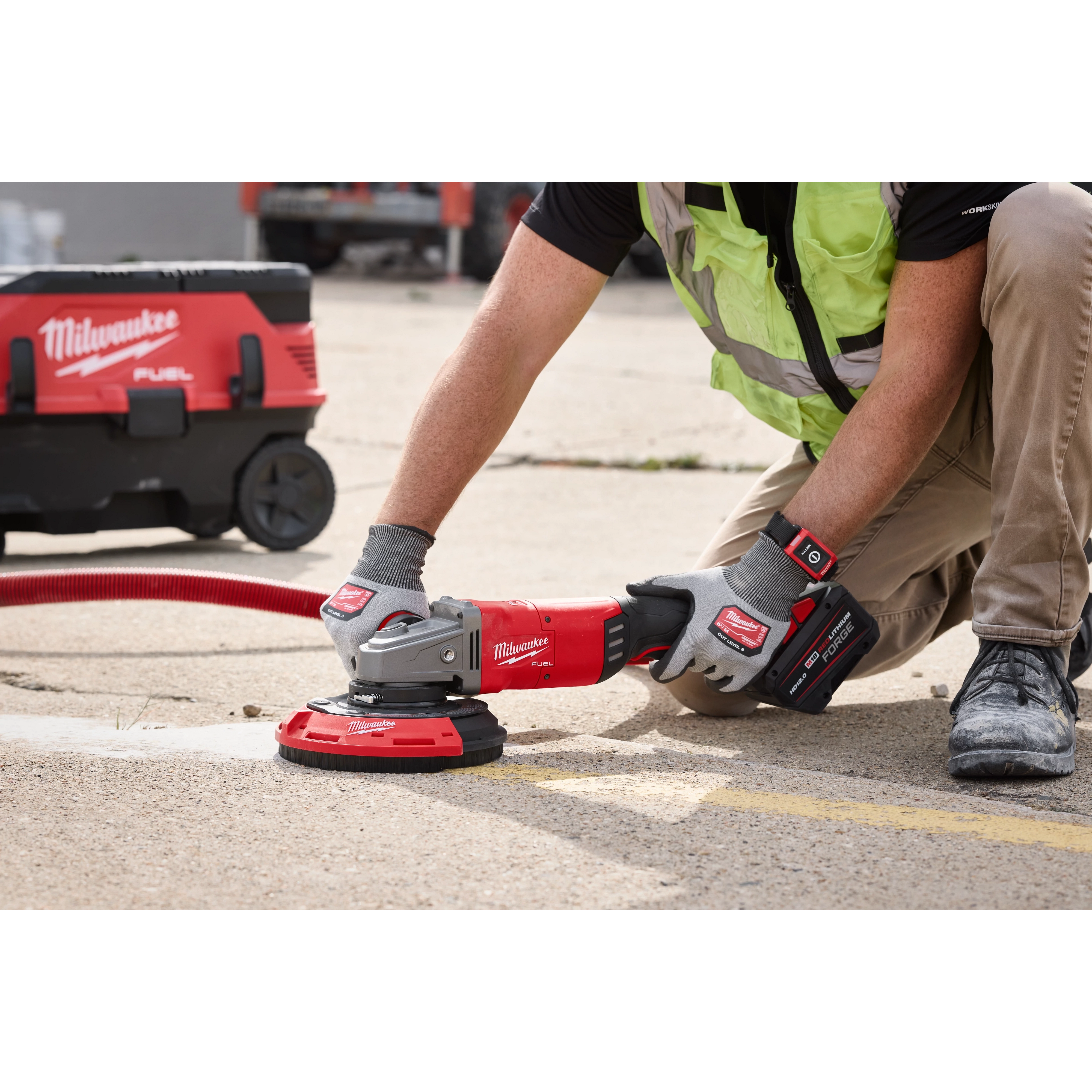 A worker uses the Milwaukee 7"/9" Surface Grinding Dust Shroud attached to a grinding tool on a concrete surface. The dust extraction vacuum is connected for debris collection.