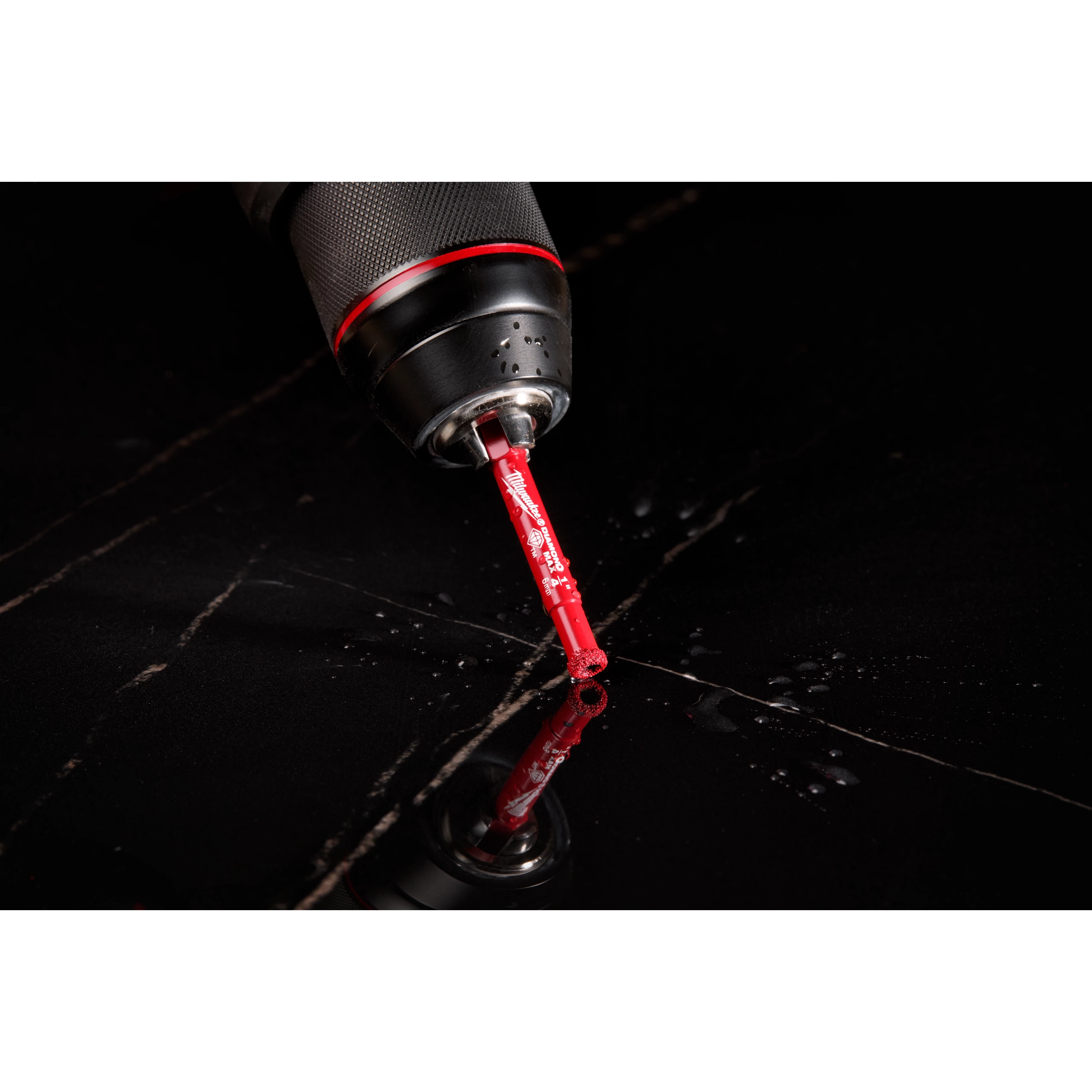 A close-up image of a Milwaukee® 1/4" DIAMOND MAX™ Hole Saw Bit attached to a drill. The red bit is positioned against a shiny black surface with droplets and reflections visible around it. The drill's black and red handle is partially visible in the frame.