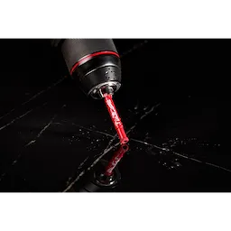 A close-up image of a Milwaukee® 1/4" DIAMOND MAX™ Hole Saw Bit attached to a drill. The red bit is positioned against a shiny black surface with droplets and reflections visible around it. The drill's black and red handle is partially visible in the frame.