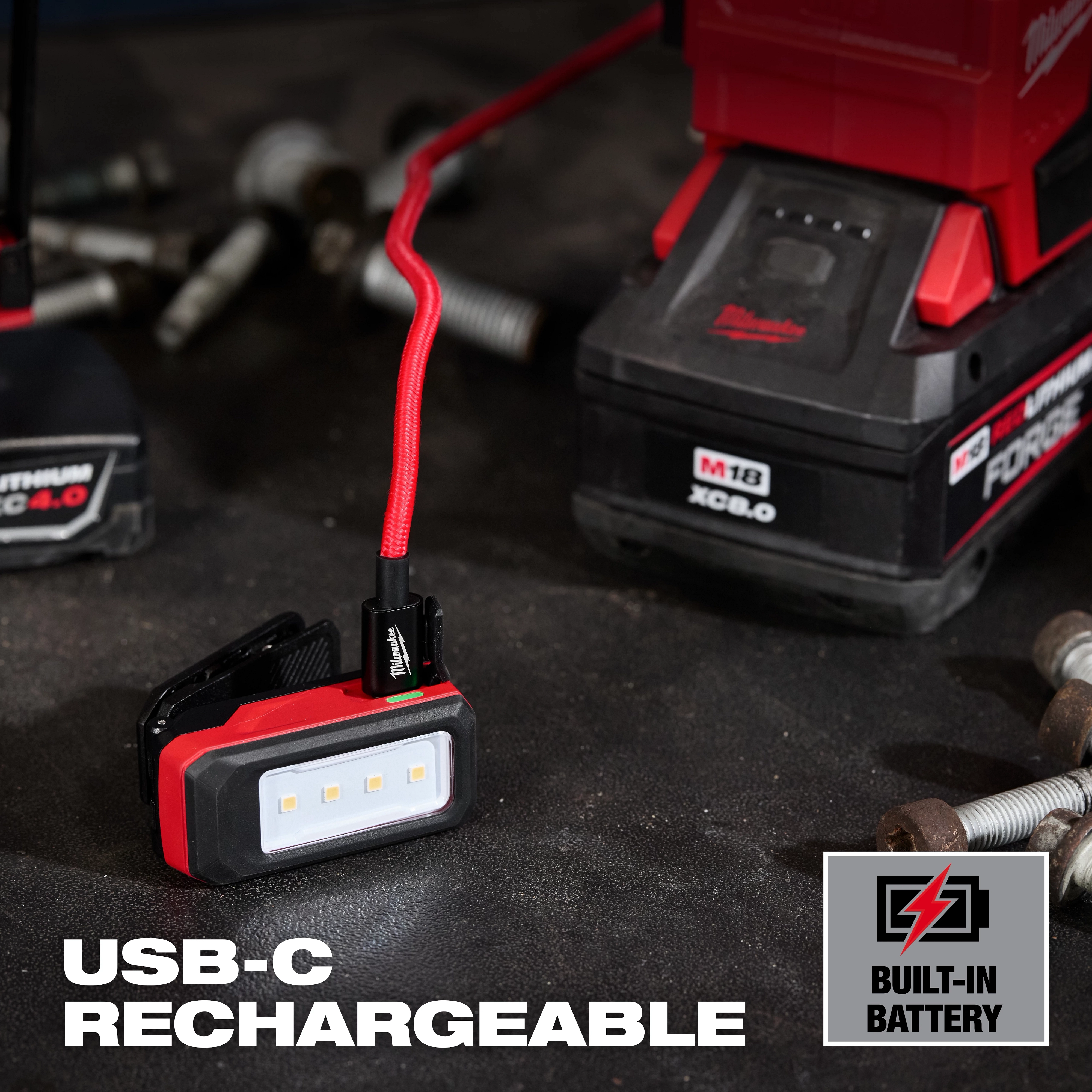Milwaukee USB-C rechargeable work light with built-in battery on a workbench near tools and bolts.