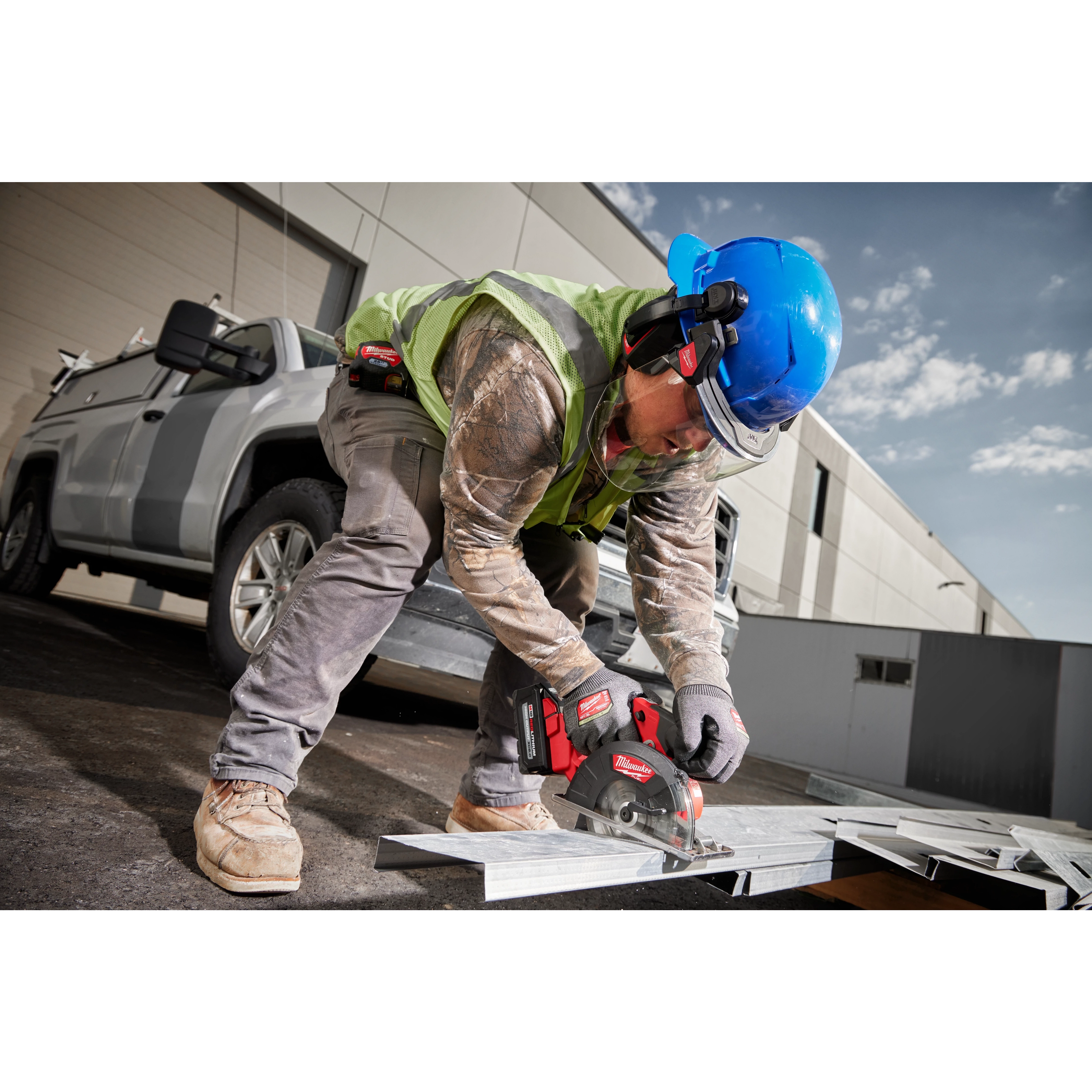 A construction worker wearing BOLT 26dB Earmuffs and a blue helmet uses a circular saw to cut metal outdoors next to a white truck.