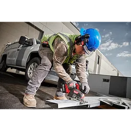 A construction worker wearing BOLT 26dB Earmuffs and a blue helmet uses a circular saw to cut metal outdoors next to a white truck.