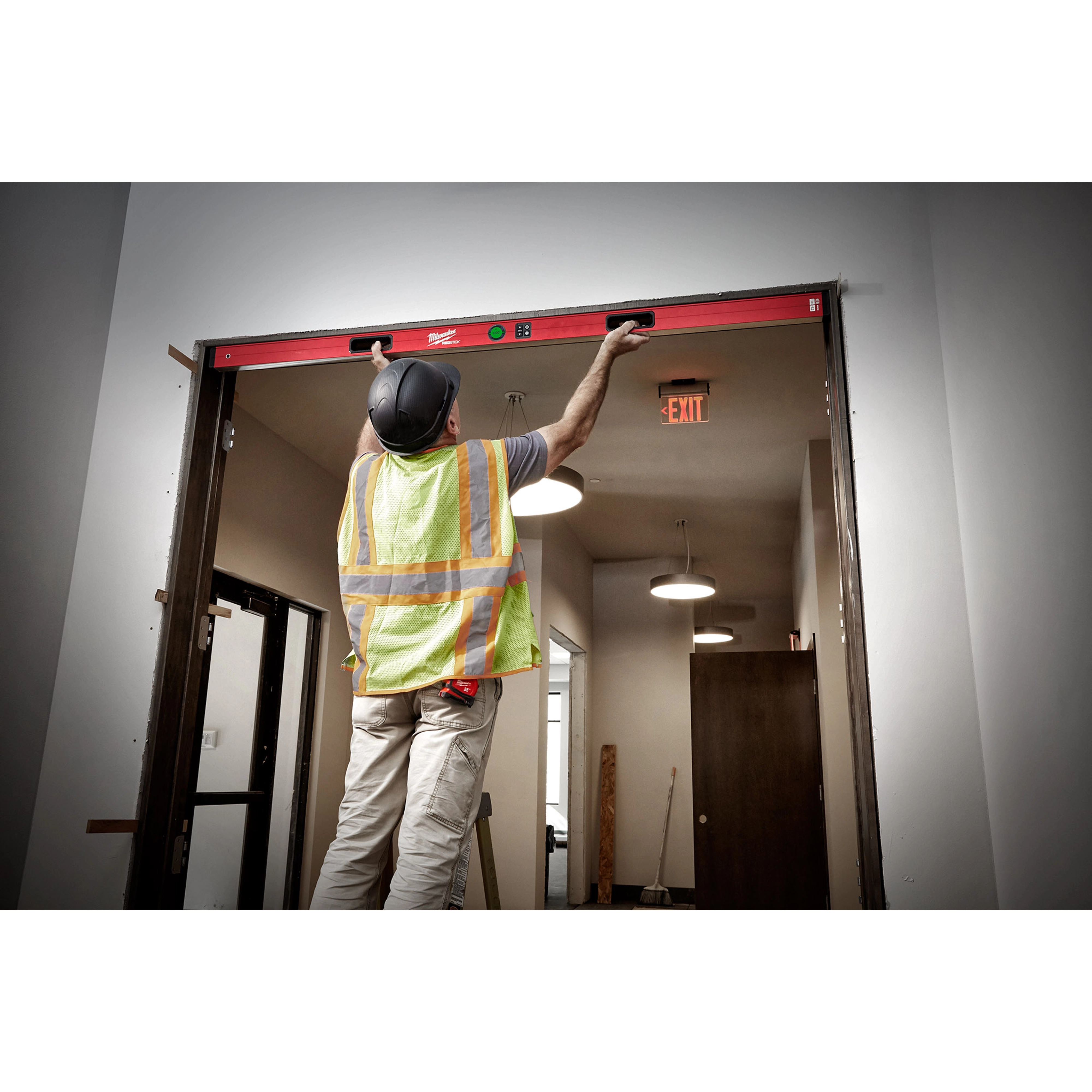 A construction worker uses the Milwaukee REDSTICK Digital Level with PINPOINT Measurement Technology to level a door frame indoors.