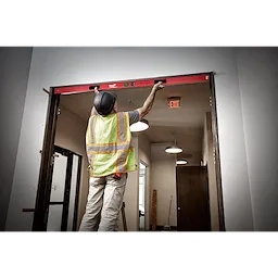 A construction worker uses the Milwaukee REDSTICK Digital Level with PINPOINT Measurement Technology to level a door frame indoors.
