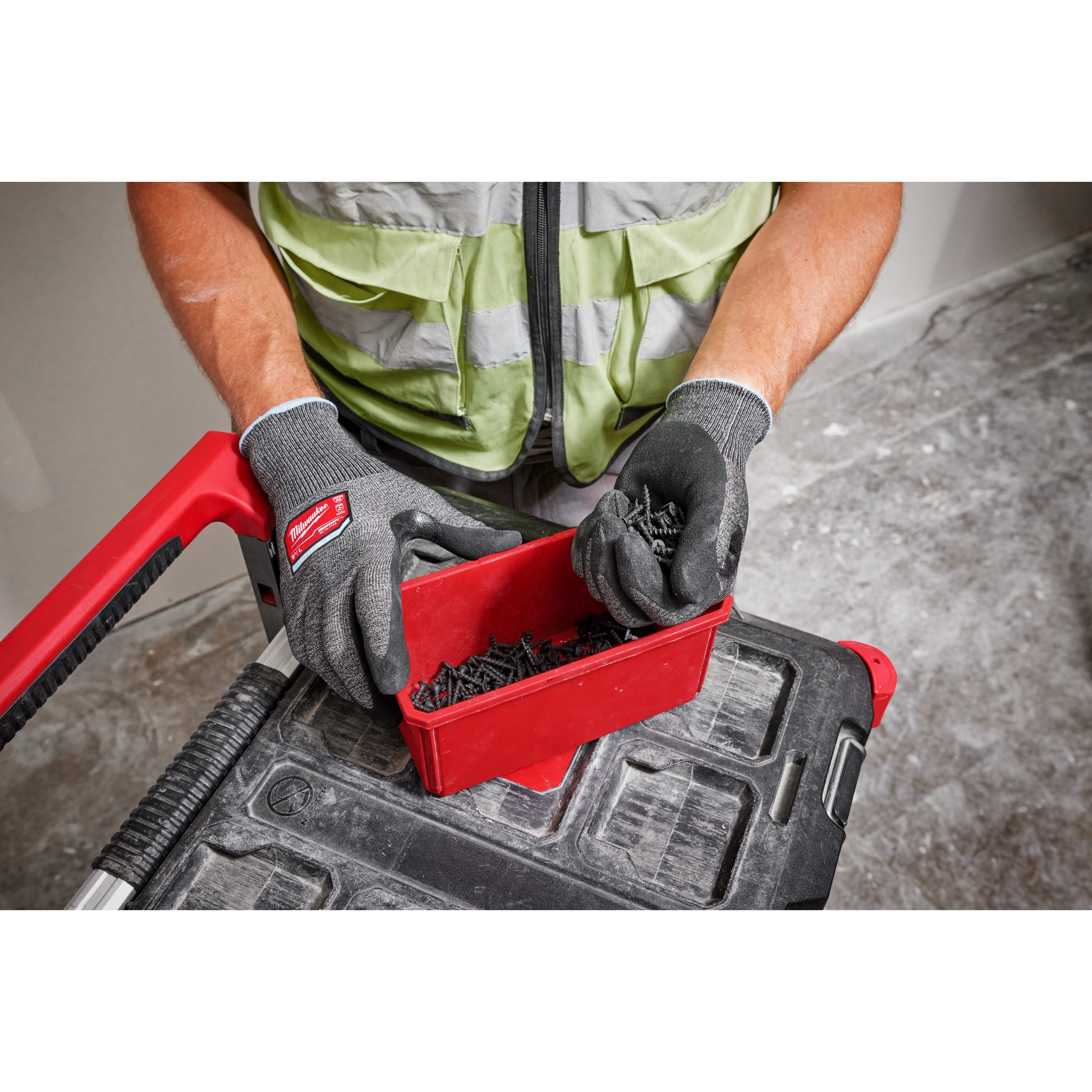 Person wearing Cut Level 2 High-Dexterity Nitrile Dipped Gloves - L handling screws from a red container on a workbench.