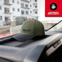 Green WORKSKIN Performance Fitted Hat with "Milwaukee" logo in black, placed on a car dashboard. Text in red: "Lightweight Breathability".