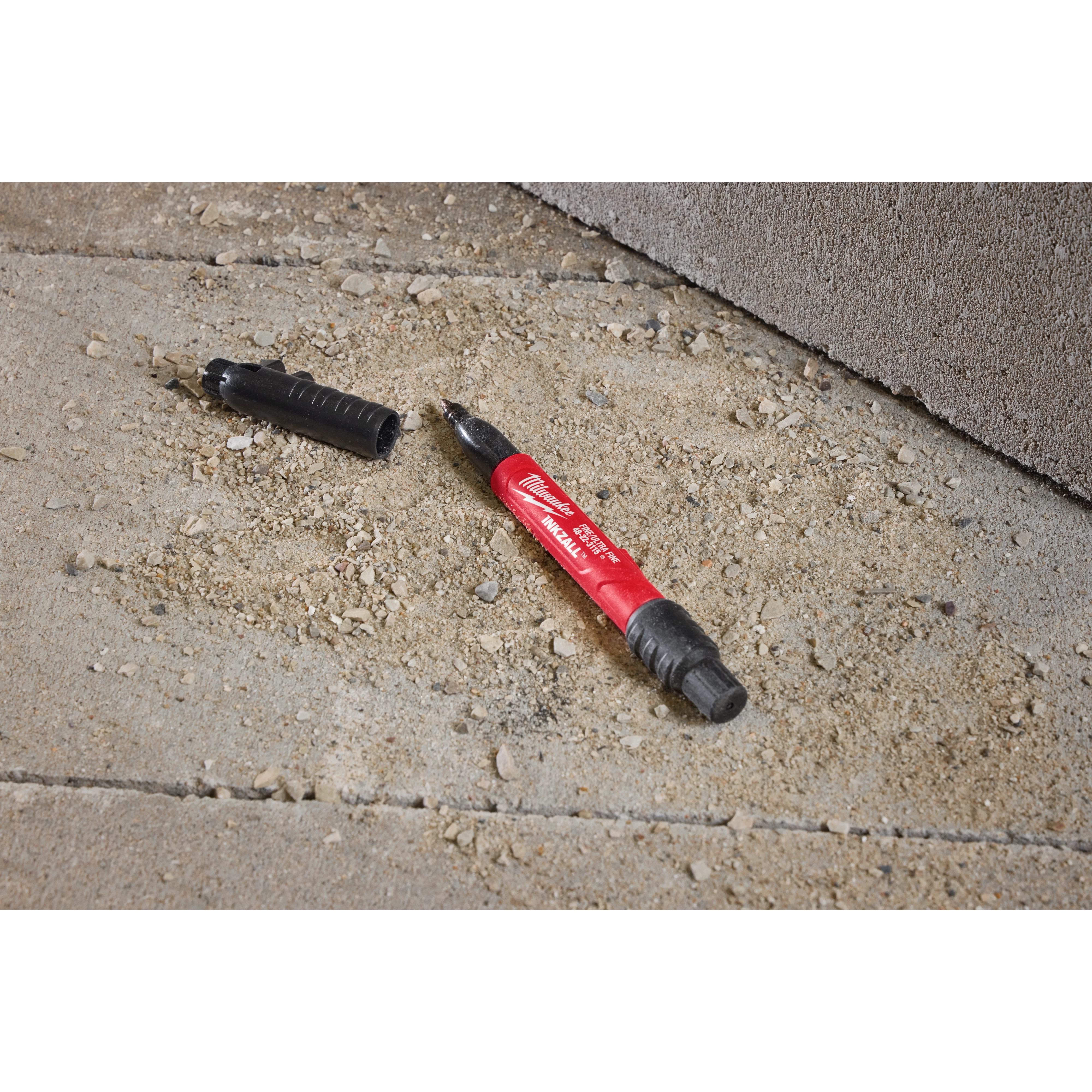 The INKZALL™ Double Sided Black Jobsite Marker – Ultra Fine & Fine Point lies on a rough, concrete surface with its cap removed, exposing the ultra-fine point.