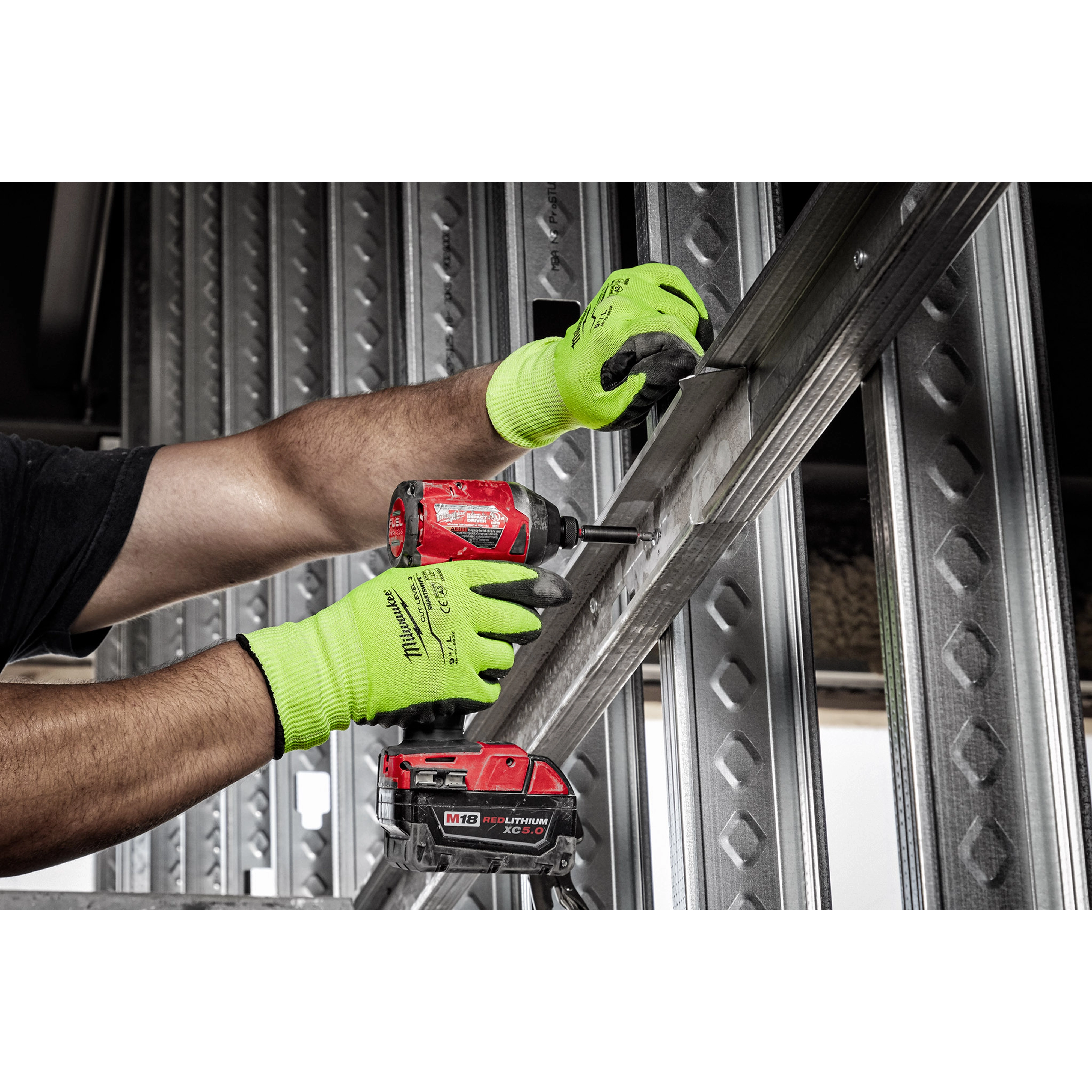 Person using a red power drill while wearing bright green Hi Vis Cut Gloves, working on metal framing in a construction setting.
