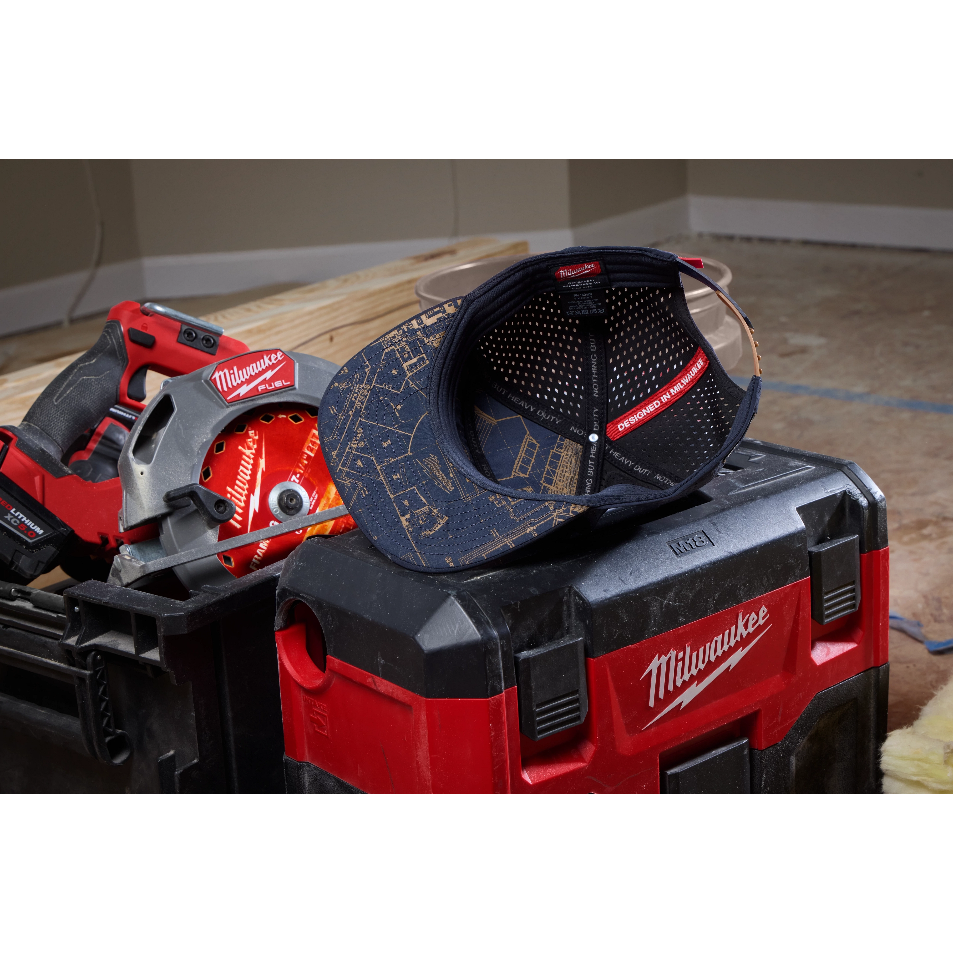 Flat Brim Snapback cap with construction pattern rests on a red and black toolbox, surrounded by power tools on a wooden surface.