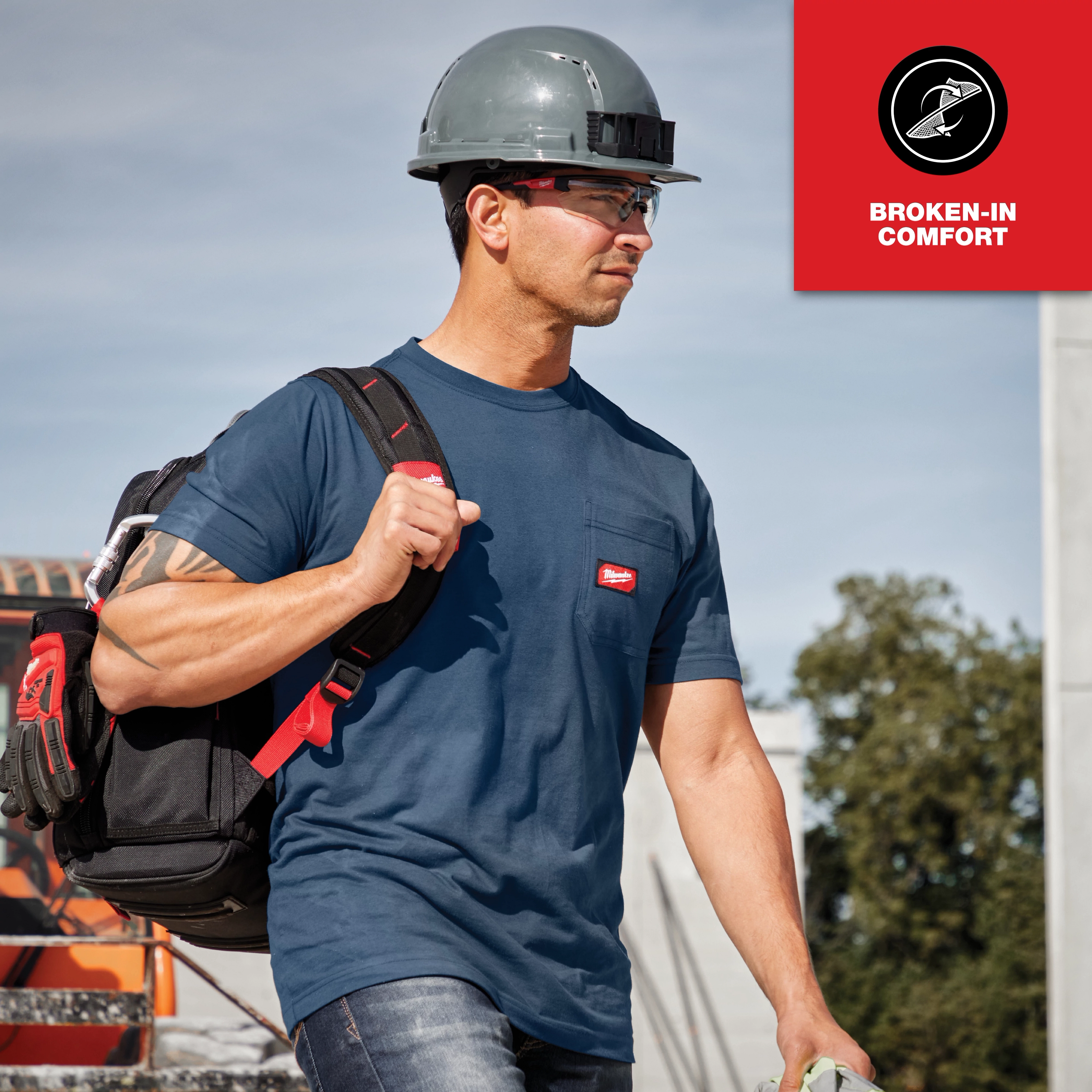 A man wearing a blue GRIDIRON Pocket T-Shirt - Short Sleeve with a helmet and carrying a backpack, labeled "Broken-in comfort".