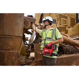Worker in safety gear using an M18 FUEL Grease Gun on large rusted construction machinery.
