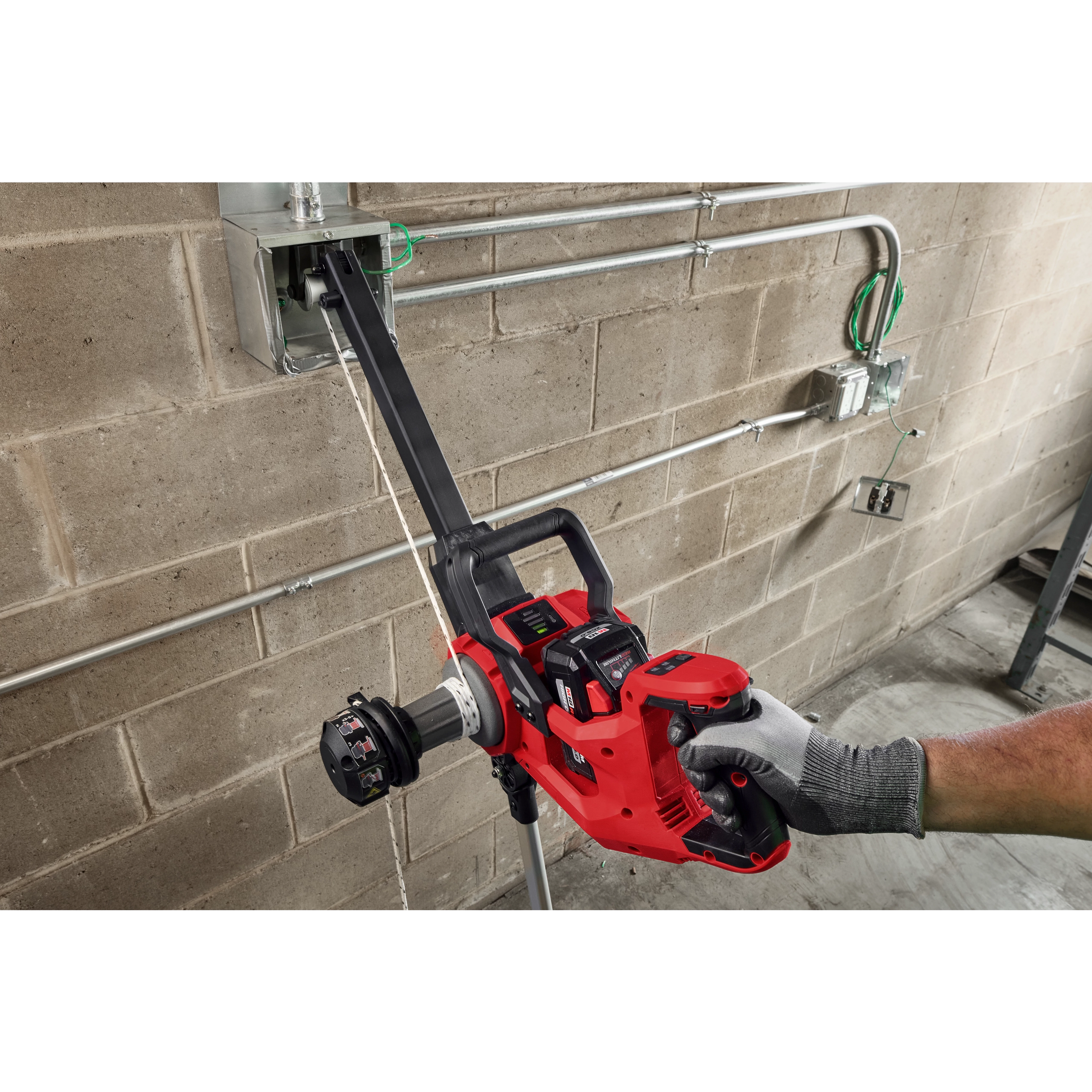 Worker using an M18 FUEL 1K Wire Puller to pull wire through conduit on a concrete wall.