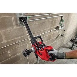 Worker using an M18 FUEL 1K Wire Puller to pull wire through conduit on a concrete wall.