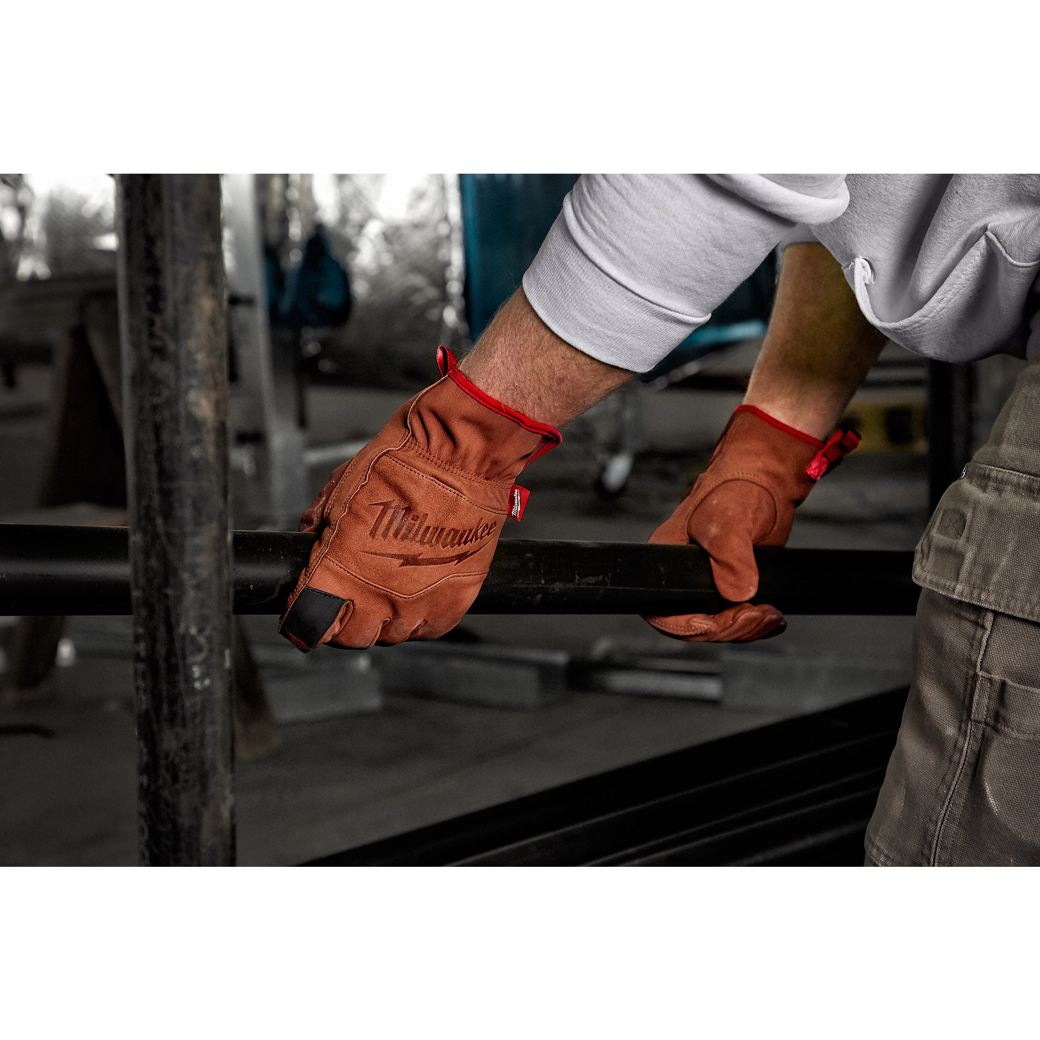 Person wearing Goatskin Leather Gloves handling a black metal pipe in an industrial setting, with red accents on the gloves.