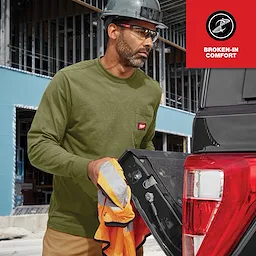 A man at a construction site wears an olive GRIDIRON Pocket Long Sleeve T-Shirt with a bright red logo. He stands next to a red pick-up truck.