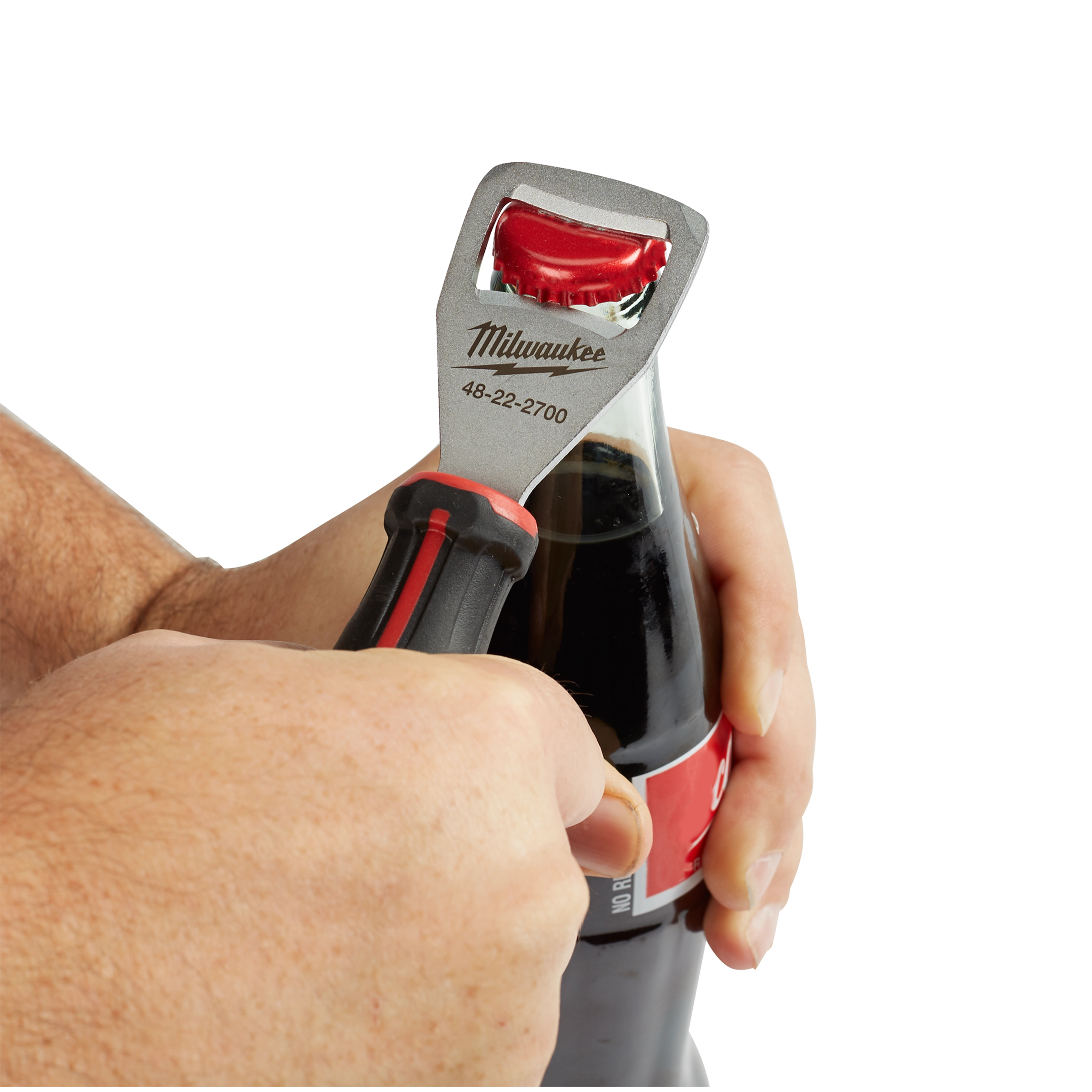 Hands using Cushion Grip Bottle Opener to open a glass soda bottle. The opener is black with red accents and silver head.