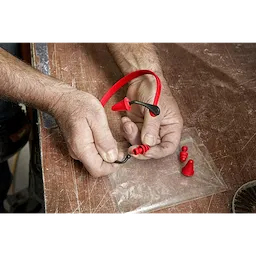 A pair of hands assembling Banded Hearing Protection, a red and black band with replaceable earplugs, on a wooden surface.