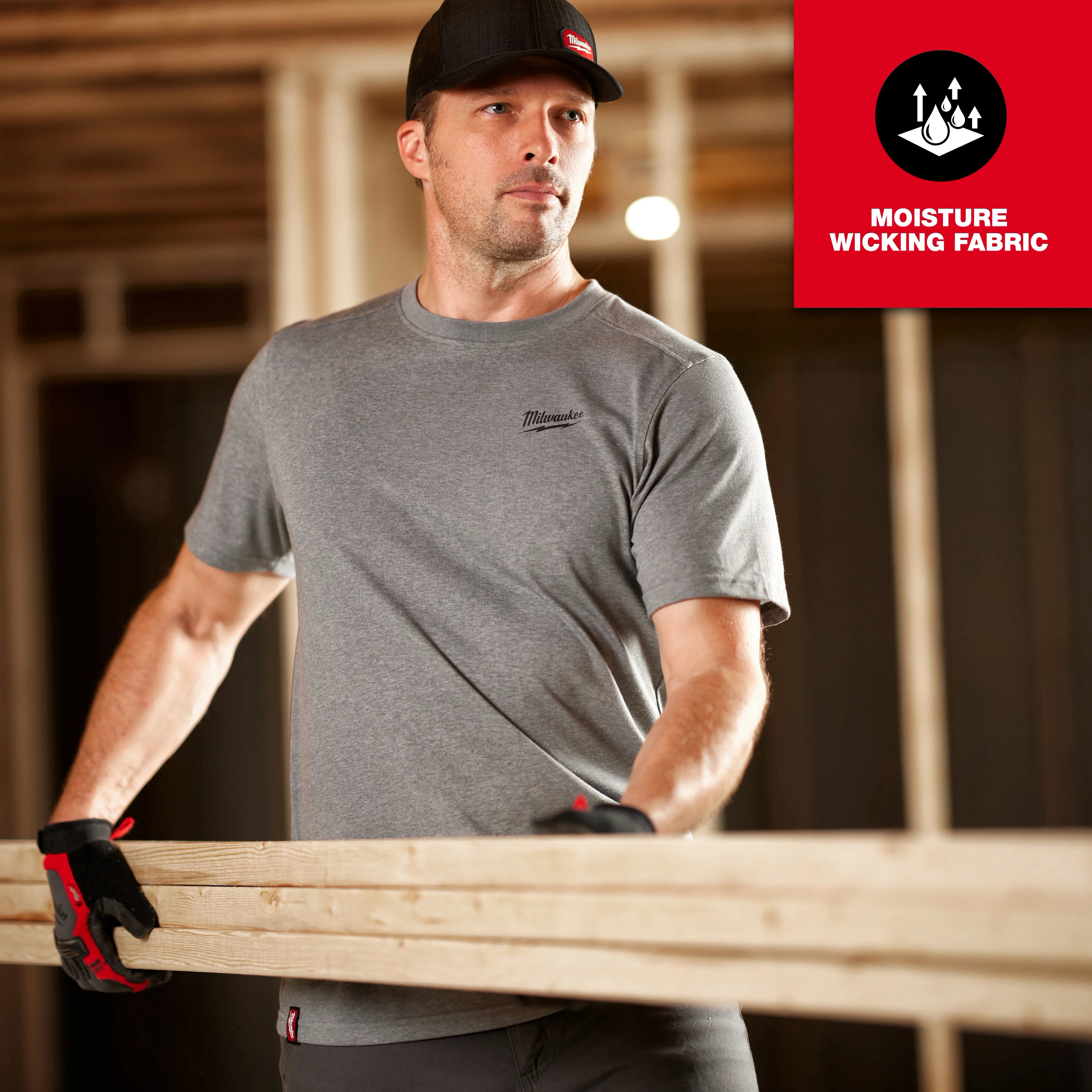 Man wearing a grey FREEFLEX Hybrid Work Tee - Short Sleeve while carrying a wooden plank, with moisture-wicking fabric text overlay.