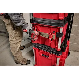 Person attaching a tool to a PACKOUT Tool Box Belt Clip Rack Attachment on a stack of red and black toolboxes.