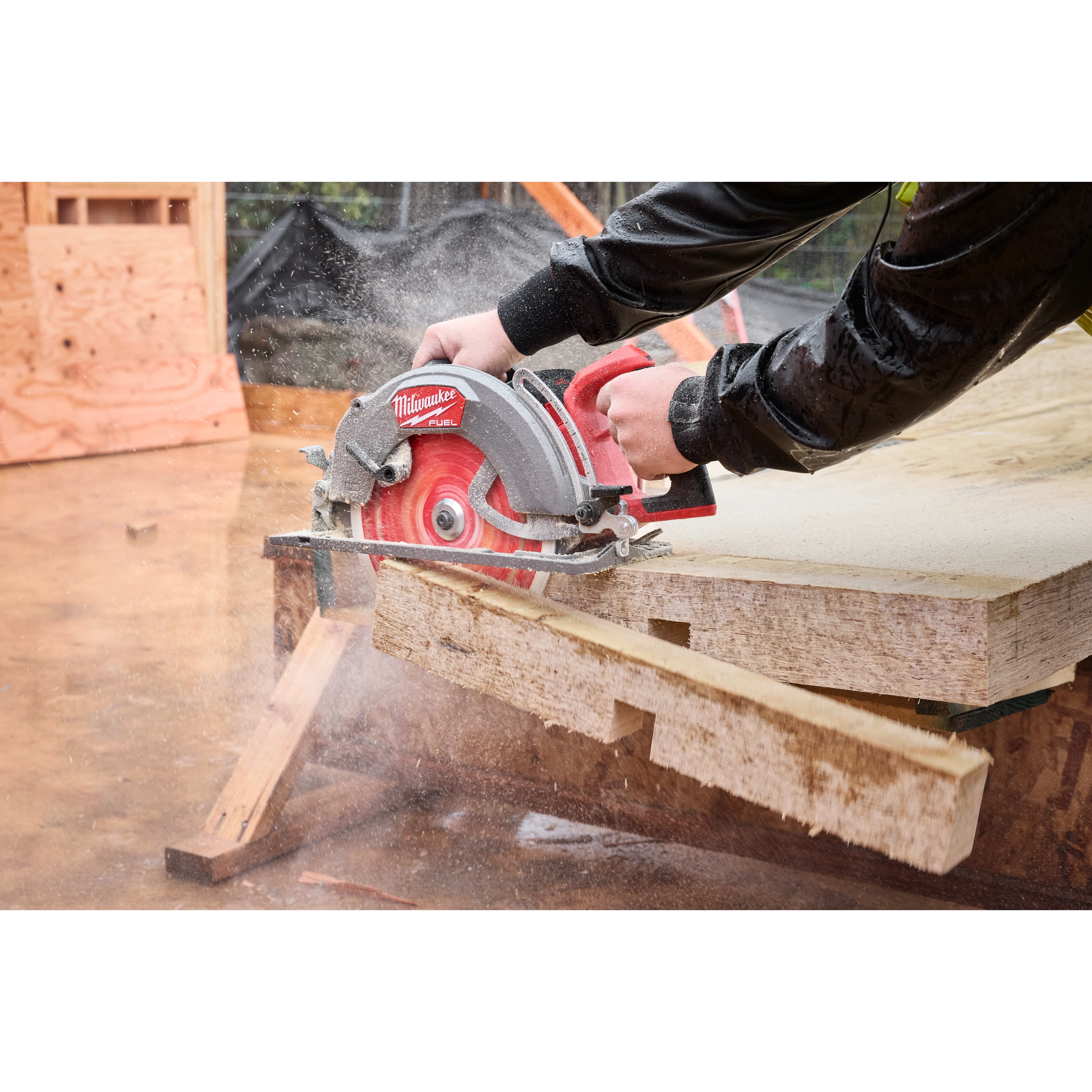 A person cutting plywood with the M18 FUEL 10-1/4" Rear Handle Circular Saw, creating sawdust and precise cuts on a construction site.