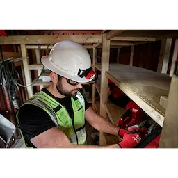 Worker wearing a BOLT White Full Brim Vented Hard Hat with 4-point Ratcheting Suspension in a wooden storage area.
