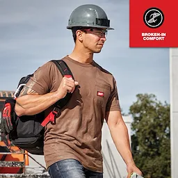 A man wearing a brown GRIDIRON Pocket T-Shirt - Short Sleeve with a tool bag, hard hat, and the text "Broken-in Comfort."