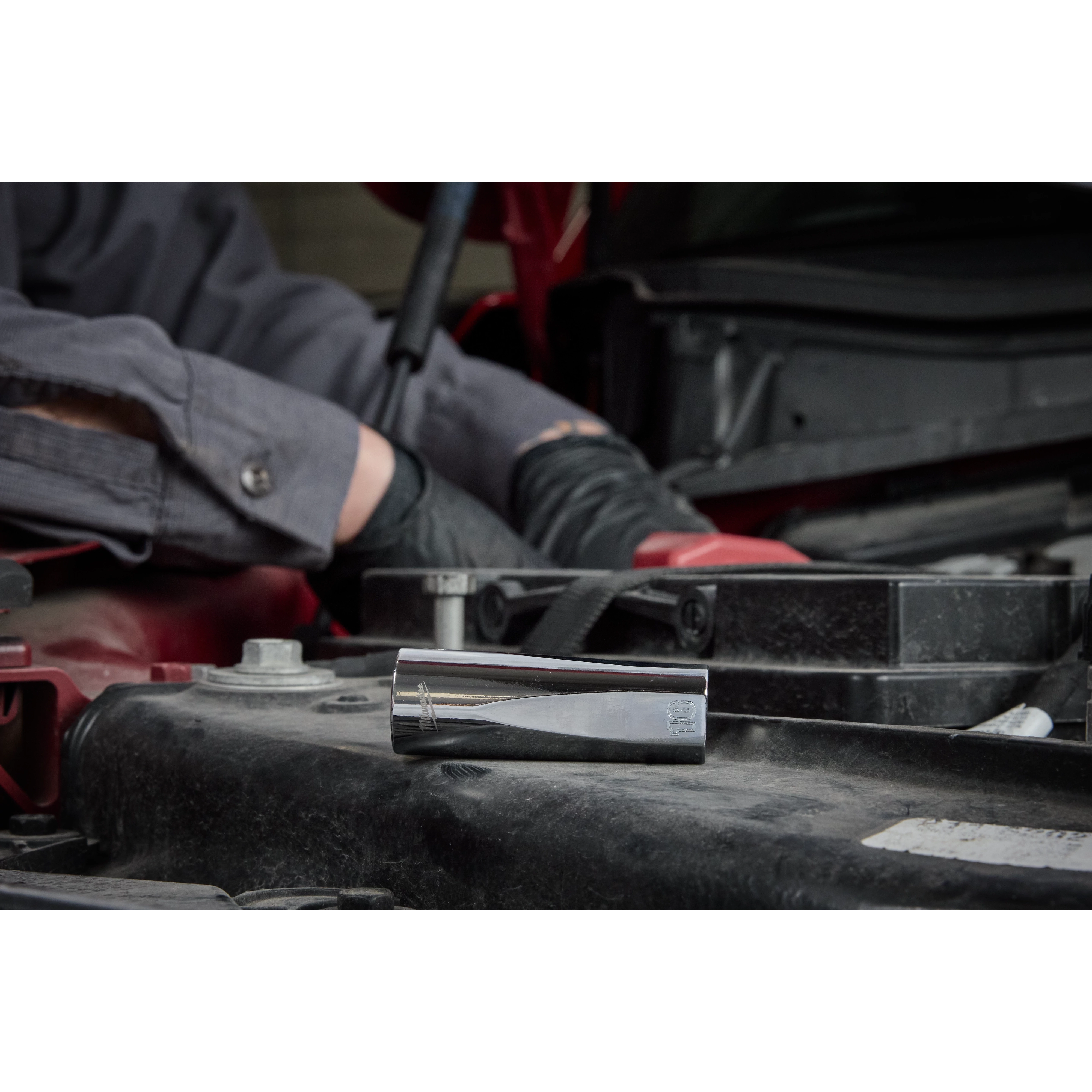 A mechanic's arm is shown working on a car engine. In the foreground, a socket tool from the 98pc 3/8" 6-Pt and 12-Pt Metric & SAE Ratchet & Socket Set with PACKOUT™ Low Profile Organizer is placed on the engine.