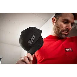 A person holding a black Milwaukee Fitted Hat, wearing a red shirt with a matching Milwaukee logo on the pocket.