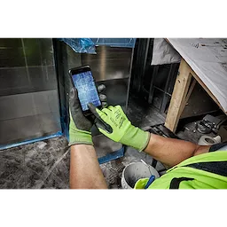 Person wearing Hi Vis Cut Gloves using a smartphone with a blueprint on the screen, in a construction worksite environment.